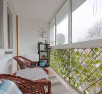 A glazed loggia in a 3-room apartment with rattan furniture and a view through greenery.