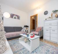 Living room in a three-room apartment with wood-patterned flooring, light furniture, and decorations.