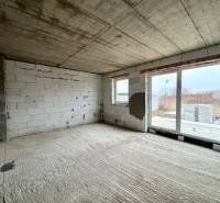 The interior of a family house with a concrete floor, raw walls, and large windows.