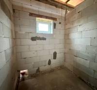 A room with a brick wall in a family house, with a small window and a concrete floor.