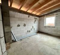 An unfinished room in a family house with a concrete floor, wooden ceiling, and a window.