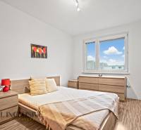 A bright bedroom with wooden decor, a flower painting, and a view of the city.