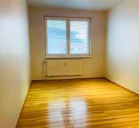 A room with a wooden decor floor in a 3-room apartment, large window, and radiator.