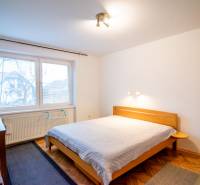 Bright bedroom in a 2-room apartment with a large window and a wood-patterned floor.