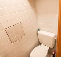 A toilet with light tiles and a shelf in a 2-room apartment.