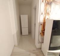 A hallway in a 2-room apartment with a wooden decor floor and a refrigerator.