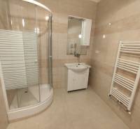 A bathroom in a 2-room apartment with a corner shower and white furniture.