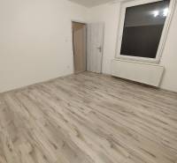 A room in a 2-room apartment with a wood-patterned floor and a large window.