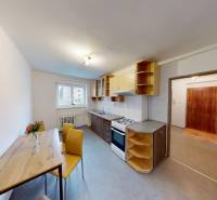 A kitchen in a 2-room apartment with a dining table, yellow chairs, a gas stove, and shelves.