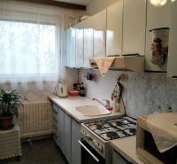 A kitchen with white cabinets, a window, a stove, and a houseplant in a 3-room apartment.