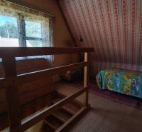 Interior of a cabin with wooden railing, a bed with colorful covers, and floral curtains.