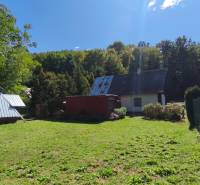 A garden with a cottage in Dolné Strháre, surrounded by forest, sunny day.