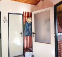 Interior of a cabin with a door, a clothes hanger, a tiled stove, and furniture.