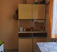 A kitchen in a cottage with a gas stove, a curtain, and cabinets.