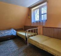 Interior of a cabin with three beds, carpet, window with a white curtain, simple furniture.