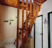 A cottage with a wooden staircase, floral curtains, and wall decorations.