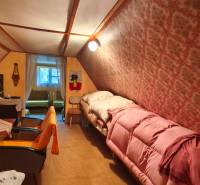 Attic room with a bed, chairs, and patterned wallpaper in a cottage.