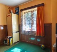 Interior of a cottage with colorful walls, a stove, and a refrigerator under a window with curtains.