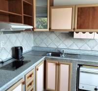 A kitchen in a studio apartment with a kitchen unit and a floor with a wooden decor.