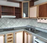 Kitchen in a studio apartment with a countertop, cabinets, and tiles on the wall.