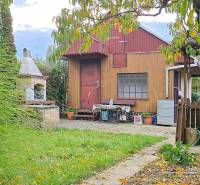 Wooden garden house with a grill surrounded by greenery and a paved walkway in Trnava.