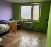A room in a 3-room apartment with a wooden decor floor, a bed, and a clothes drying rack.