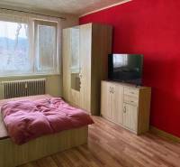 A bedroom in a 3-room apartment with a red-colored wall, a wooden decor floor, and furniture.