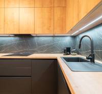 A kitchen in a 3-room apartment with contrasting dark tiles and backlighting, and a floor with a wooden decor.