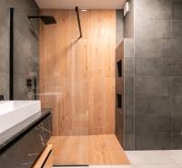 A bathroom with a shower, wooden decor flooring, and dark tiles in a 3-room apartment.