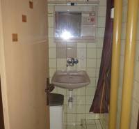 Bathroom in a studio apartment with a sink and a shower in beige tiles.