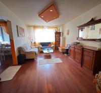 Living room in a three-room apartment with wood-patterned flooring and comfortable seating.