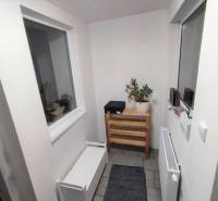 A narrow hallway with white furniture and a wooden shelf in a family house.