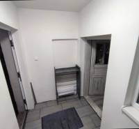 The interior of a family house with tiled flooring and white walls leads to wooden doors.