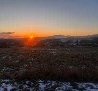 Sunset over family houses in Tvrdomestice with hills in the background.