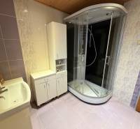 A bathroom in a family house with tiles, a shower corner, and white furniture.