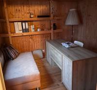 A room in a family house with wooden paneling, a sofa, a table, and shelves.