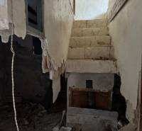 The staircase leads to the upper floor in the interior of a family house with plaster in a dilapidated condition.