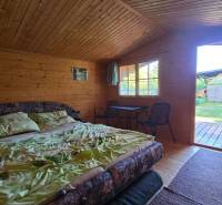 A wooden cabin with a bed, a table, and a view of the garden.