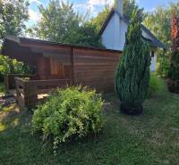 A wooden cottage in the village of Úľany nad Žitavou surrounded by green shrubs and trees.
