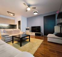 Living room of a two-room apartment with a wooden decor floor, kitchen, and comfortable sofas.