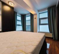 A bedroom in a two-room apartment with a wooden decor floor and large windows.