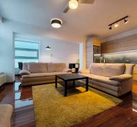 Living room in a two-room apartment with a wooden decor floor, light sofas, and a kitchen unit.