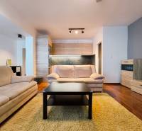 Living room in a two-room apartment with sofas, wood-decor flooring, and a kitchenette.
