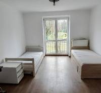 A room in a 2-room apartment with two single beds, a table, and a floor with a wooden decor.