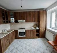 A kitchen with wooden cabinets, white walls, and orange chairs in a two-room apartment.