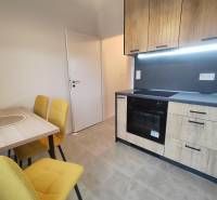 A kitchen in a studio apartment with wooden cabinets, a dining table, and yellow chairs.