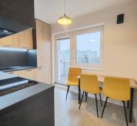 A kitchen in a studio apartment with a wood-patterned floor and yellow chairs.