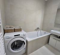 A bathroom with a bathtub, sink, and washing machine in a 3-room apartment.