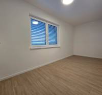 A room in a 3-room apartment with a wooden decor floor and a window with blinds.