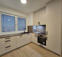 A kitchen with a wooden decor floor in a 3-room apartment, light cabinets, and built-in appliances.